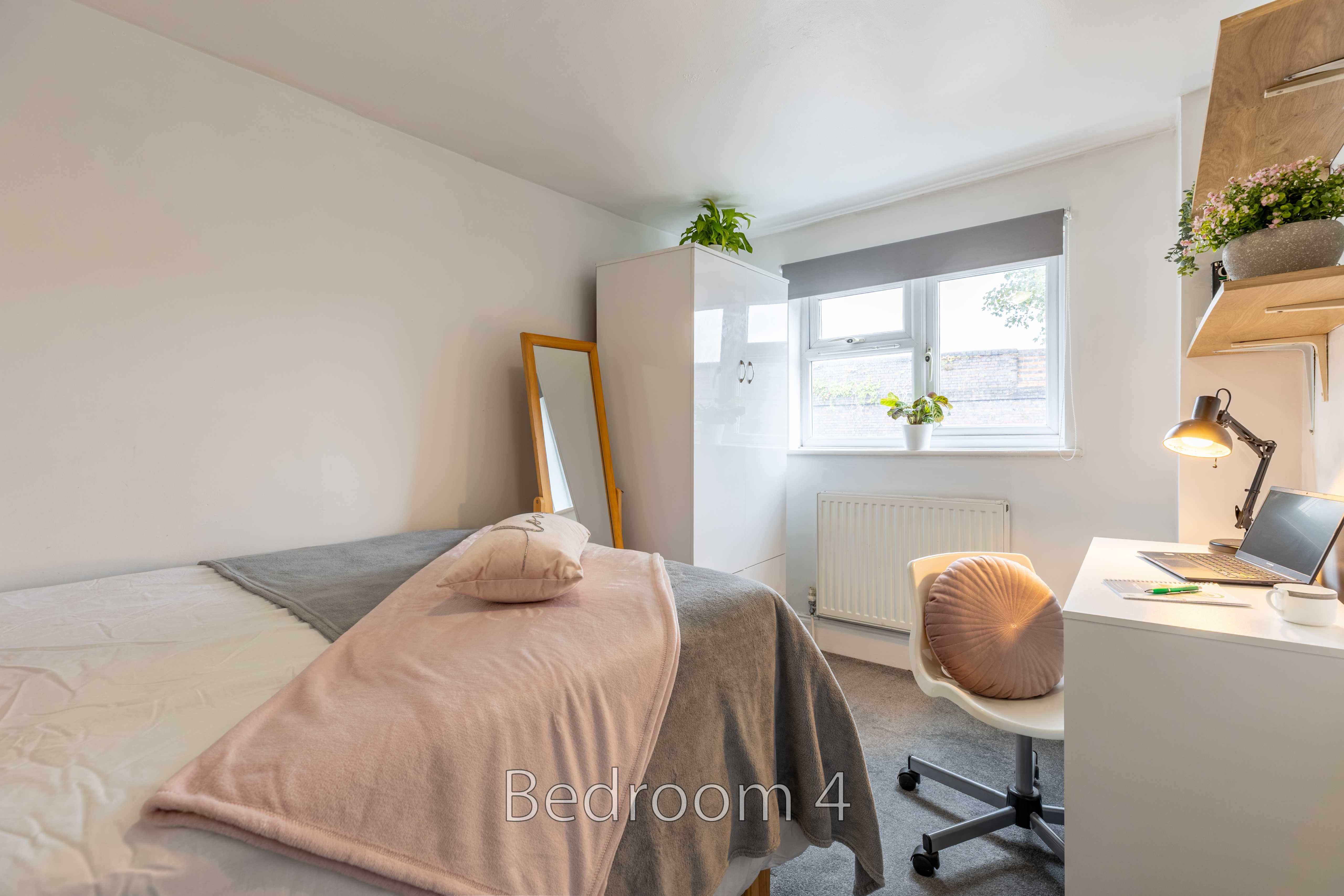 A bright bedroom with a single bed, desk, chair, wardrobe, mirror and window.