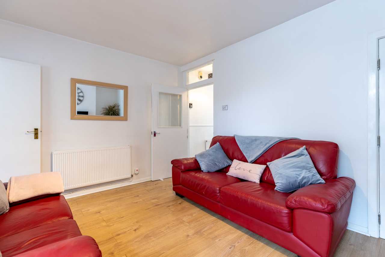 A bright living room with red leather sofas, cushions, a radiator, wooden flooring and white doors.