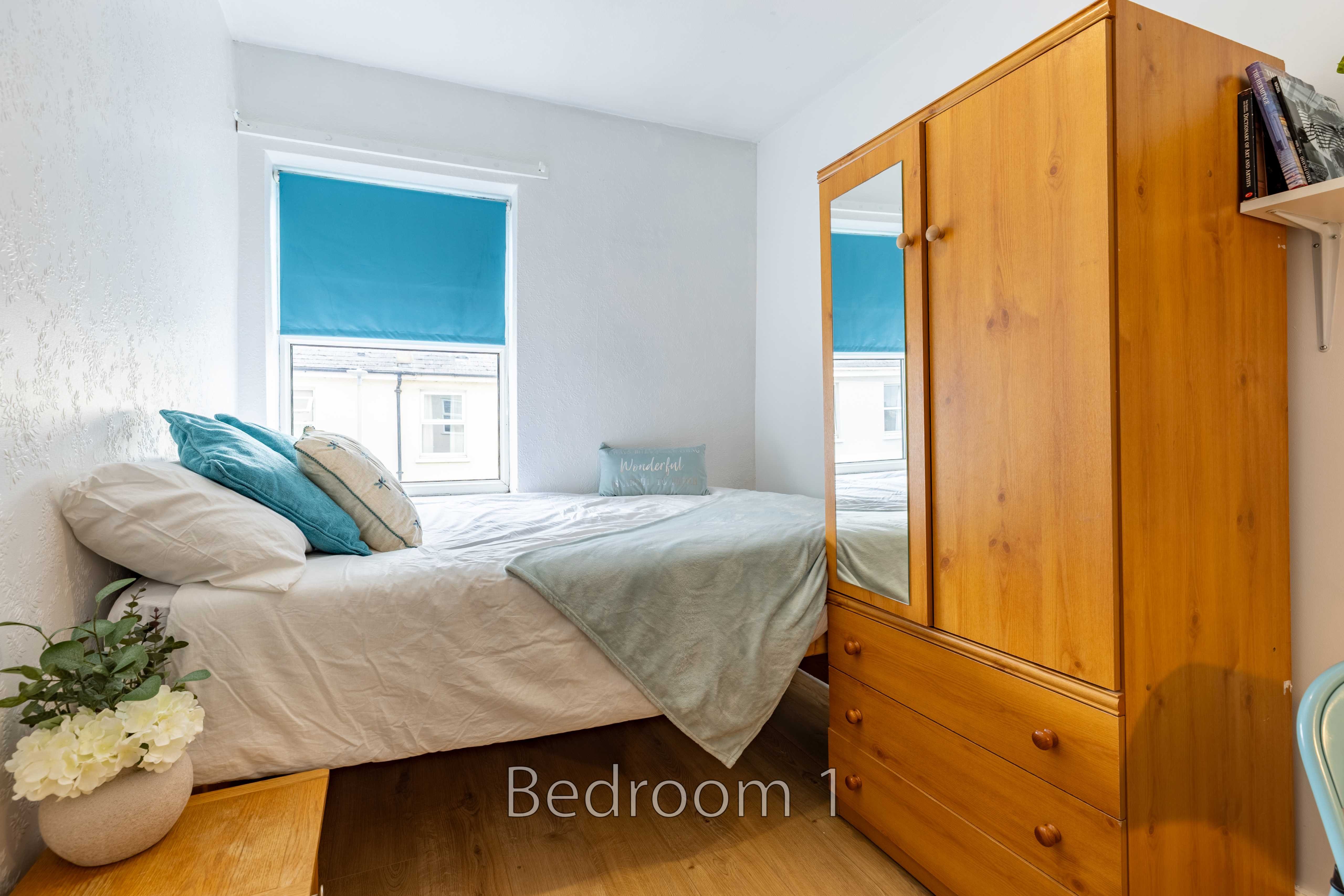 A single bedroom with a bed, pillows, a window, and a wooden wardrobe.