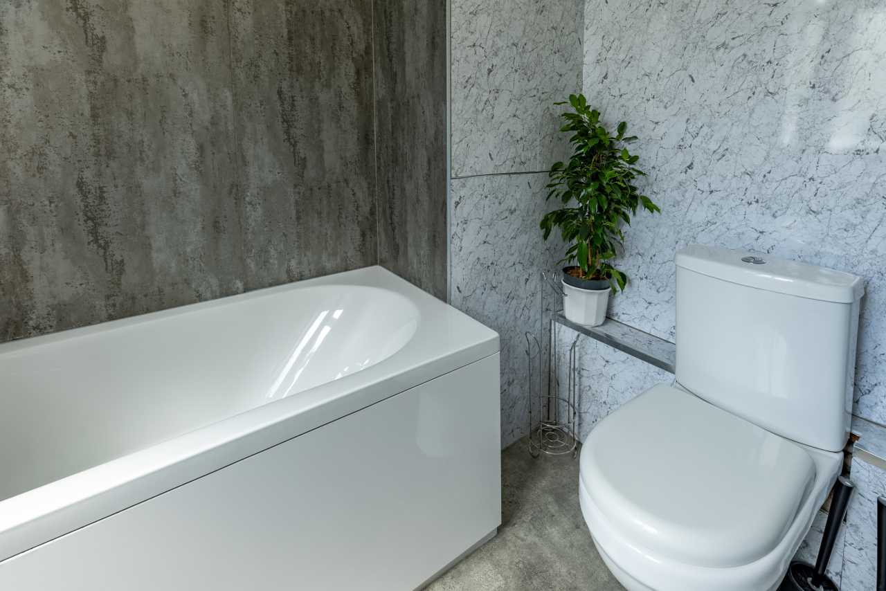 A modern bathroom with a white bathtub, toilet, tiled walls, and a potted plant.