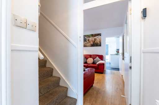 Interior view showing a carpeted staircase beside a doorway, with a red sofa and wooden flooring visible beyond.