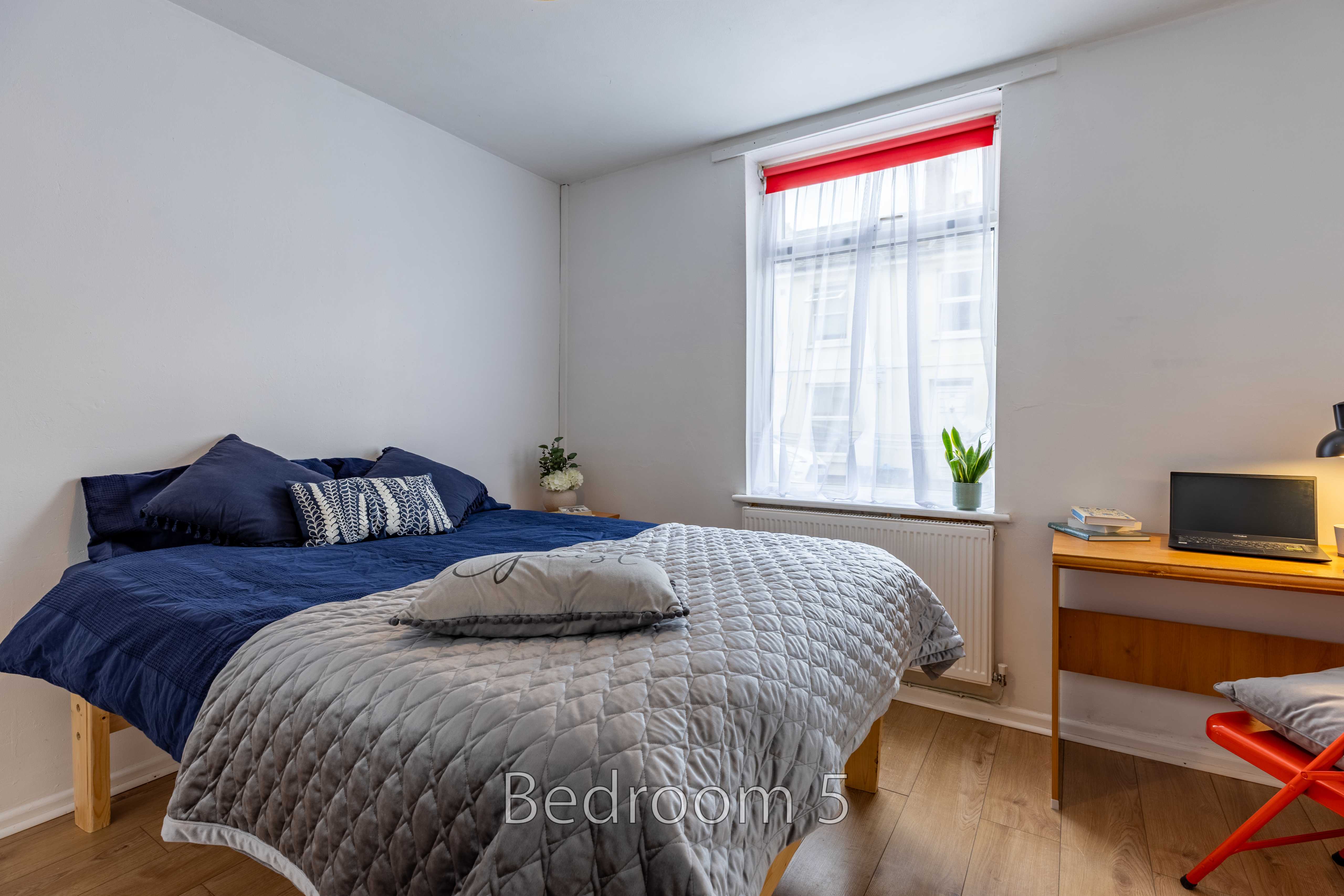 Bedroom with a double bed, window, desk, television and wooden flooring.
