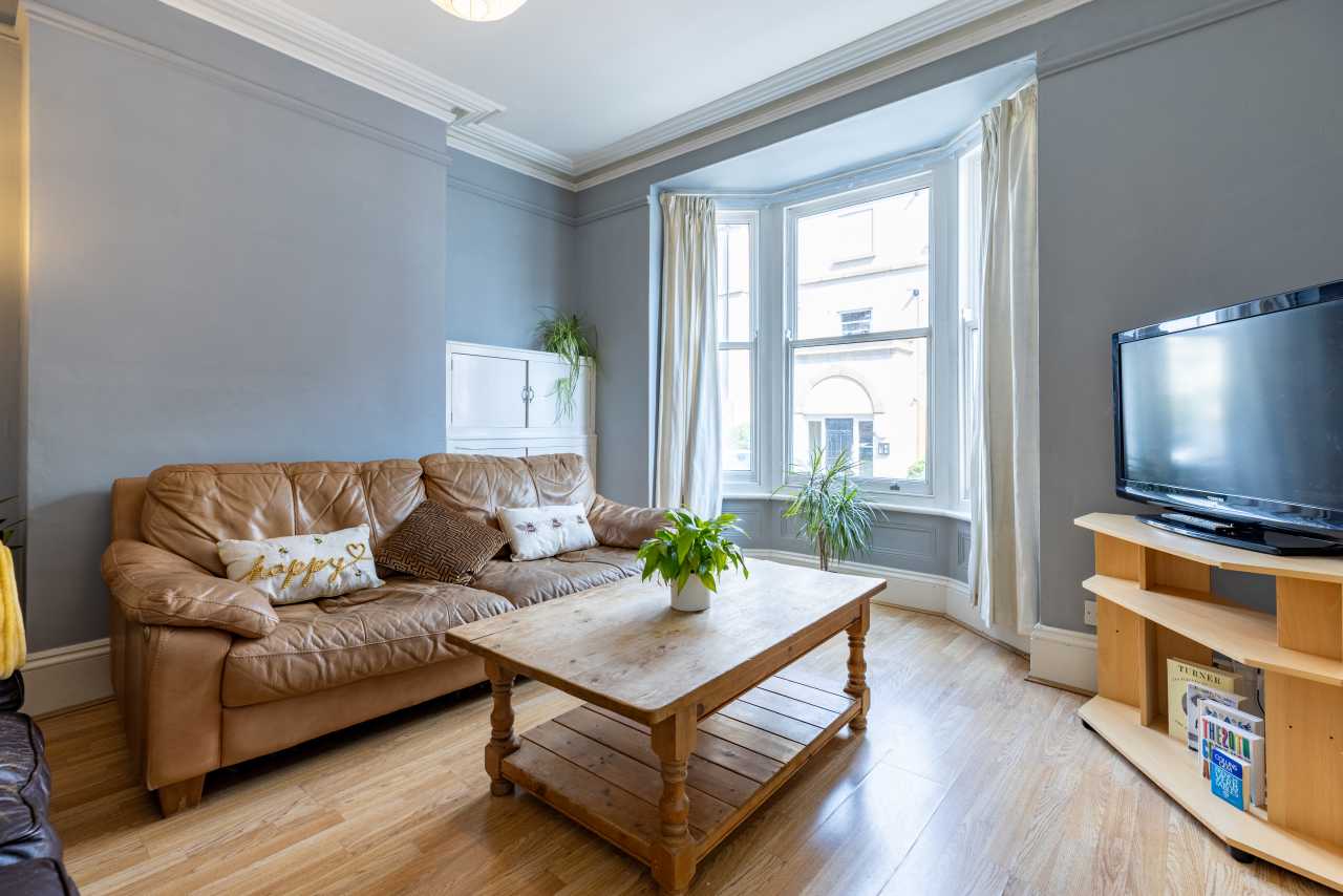 Furnished living room with a leather sofa, coffee table, television, bay window and wooden flooring.