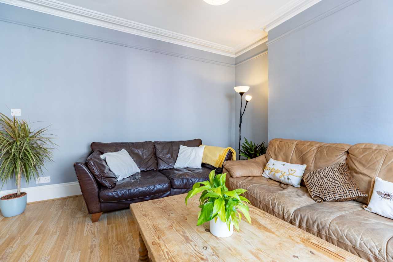 A furnished living room with two sofas, a wooden coffee table, potted plants and pale blue walls.