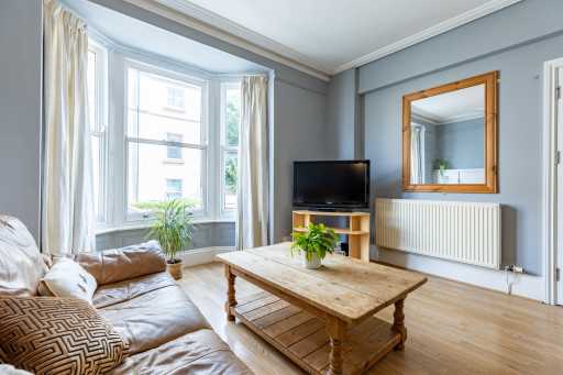 Bright living room with a bay window, sofa, television, coffee table, radiator and wall mirror.