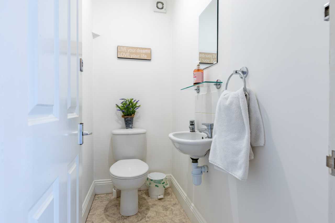 Small white toilet room with a toilet, pedestal sink, mirror, towel and beige patterned flooring.