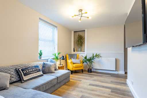 Bright living room with a large grey sectional sofa, yellow armchair, plants, radiator, television and wood-effect flooring.