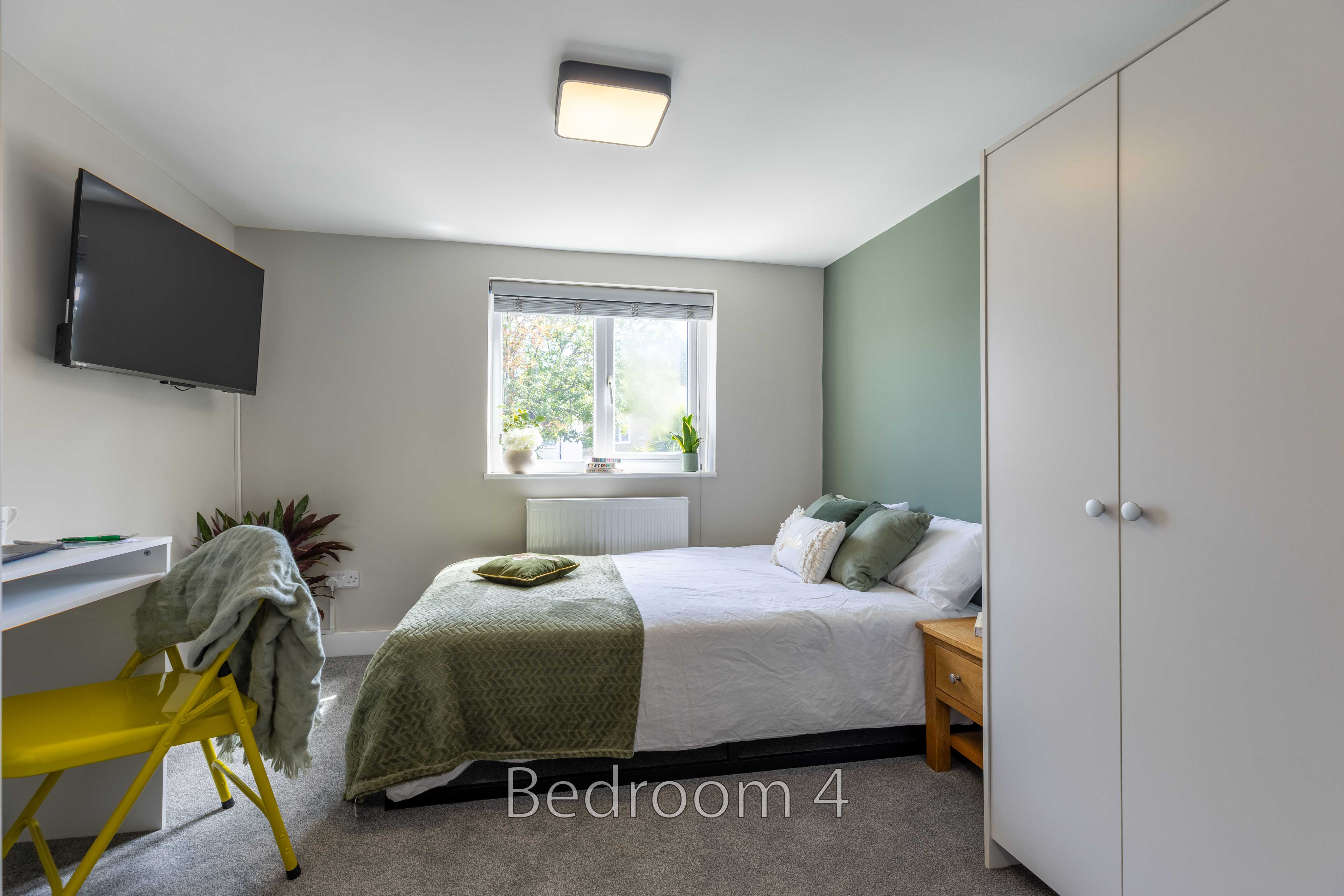 A furnished bedroom with a double bed, wardrobe, desk, chair, television and window.