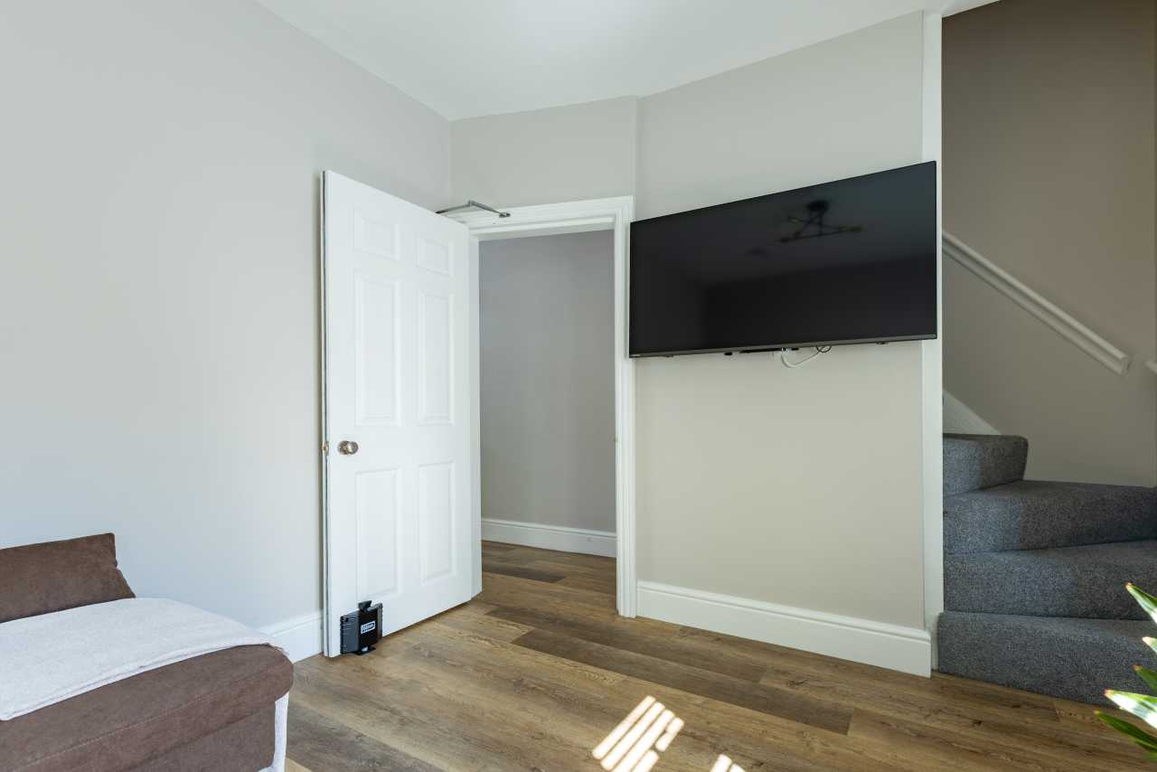 Bedroom with a bed, wall-mounted television, open door and carpeted staircase.
