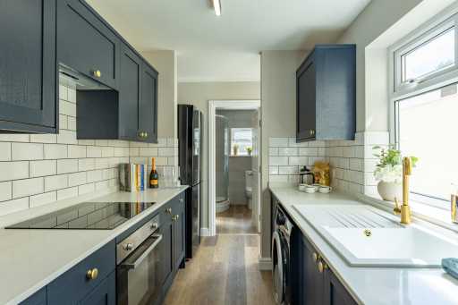 Modern galley kitchen with dark cabinets, white tiled backsplash, countertops, sink, oven and windows.