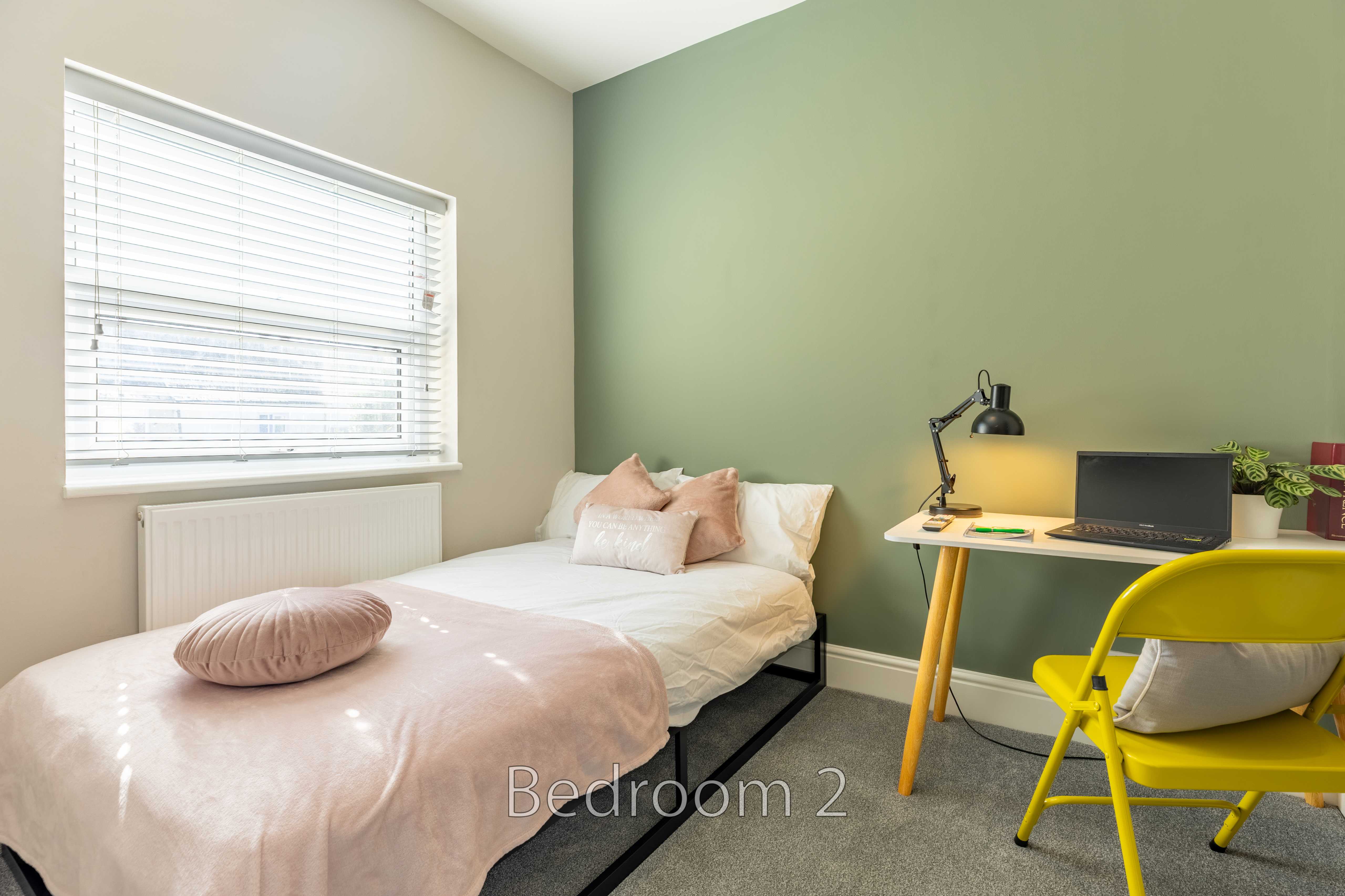 A bedroom with a single bed, desk, chair, window and radiator.