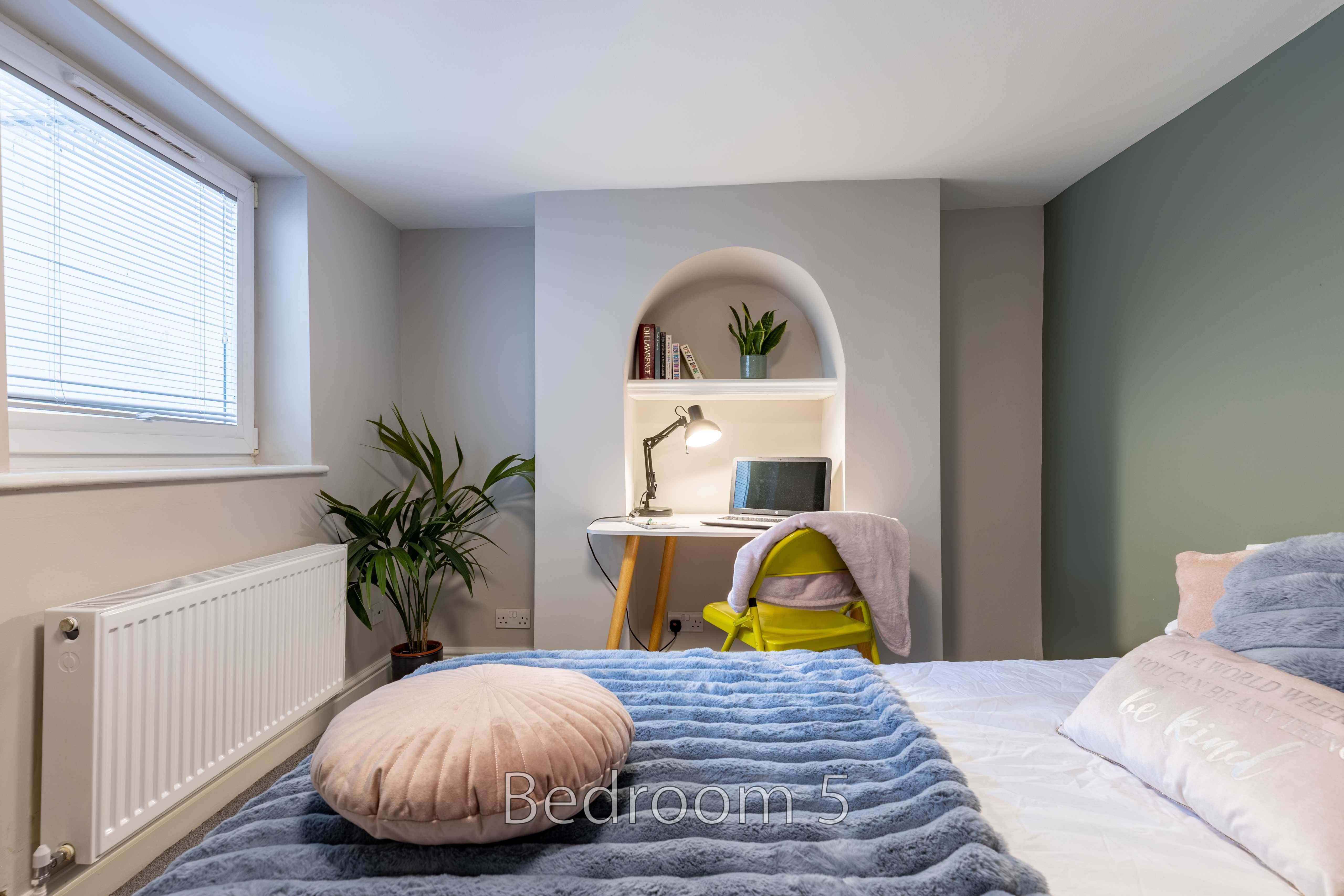 A furnished bedroom with a bed, desk, shelving, window and radiator.