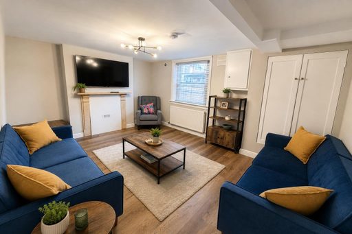 Living room with two blue sofas, a fireplace, television, rug and storage cupboards.