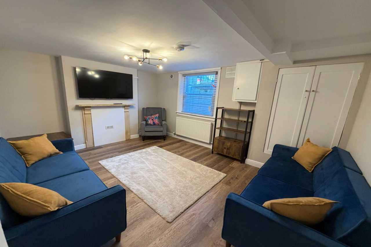 Living room with two blue sofas, a fireplace, television, rug and storage cupboards.
