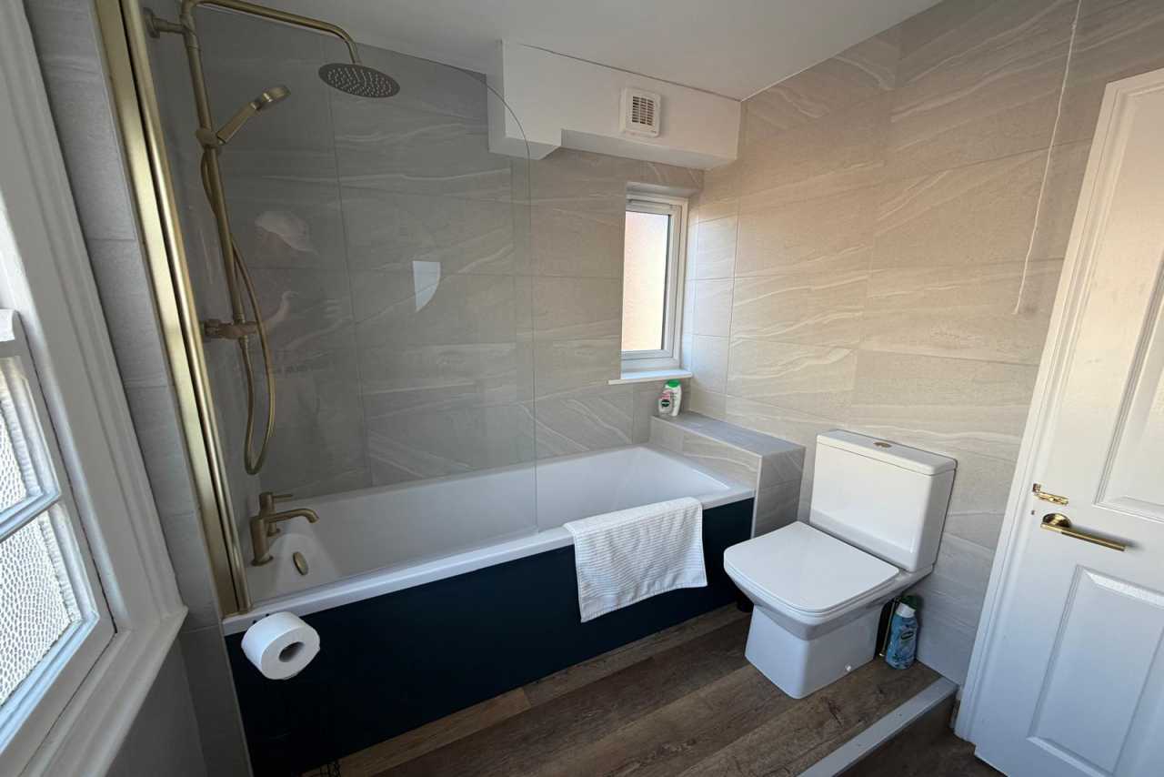 A tiled bathroom with a bathtub, shower, toilet, sink, window and white door.