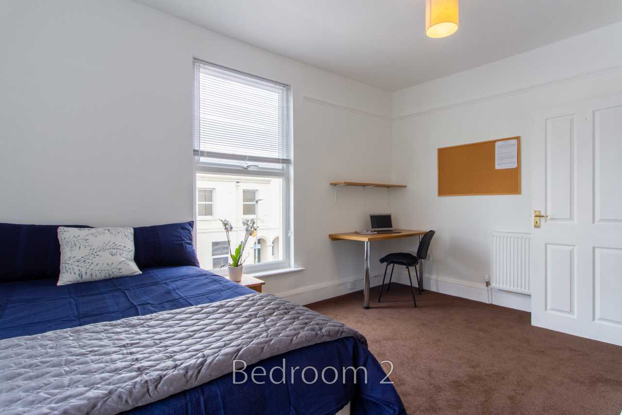 A bedroom with a blue bed, desk and chair, window, radiator and white door.